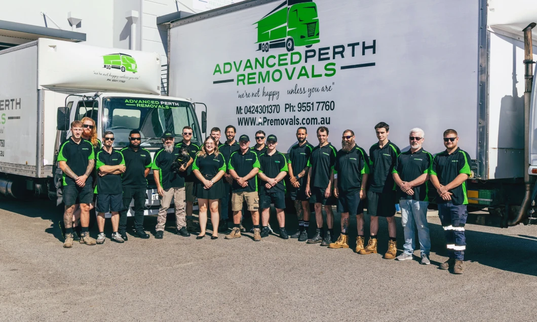 A team of removalists in green-and-black uniforms standing in a line in front of an Advanced Perth Removals truck with the company logo on the side.
