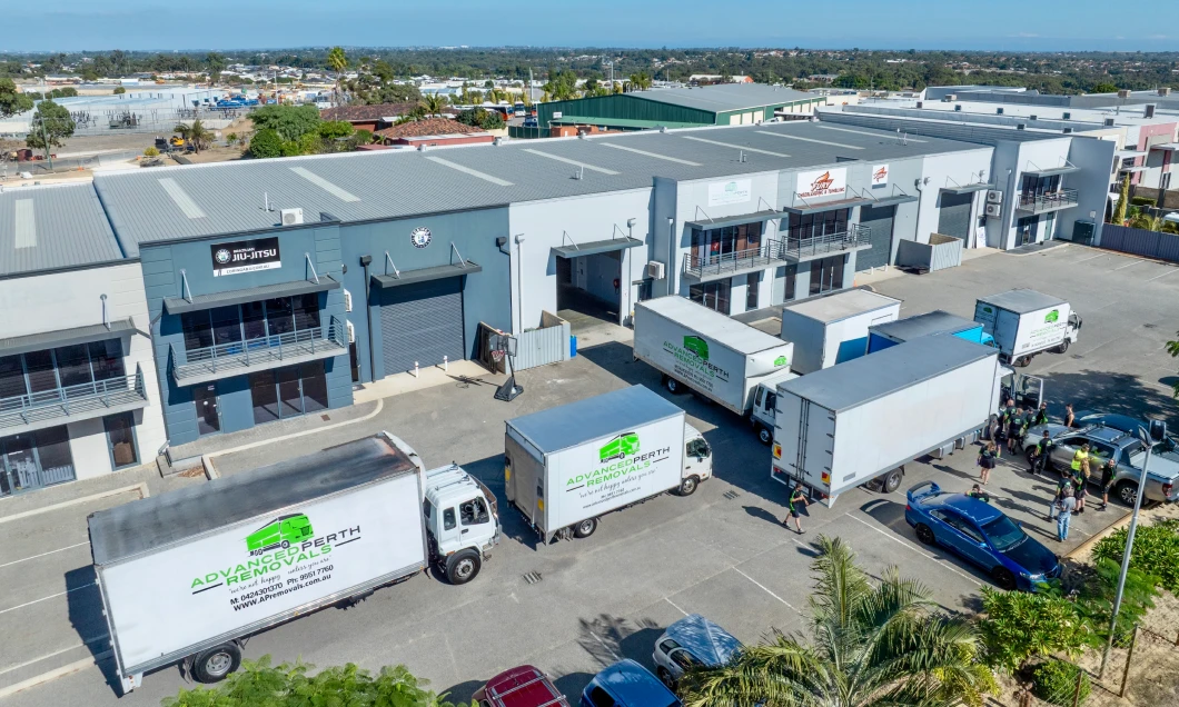 Aerial view of a gray industrial park with loading bays and several Advanced Property Removals moving trucks parked at the docks.
